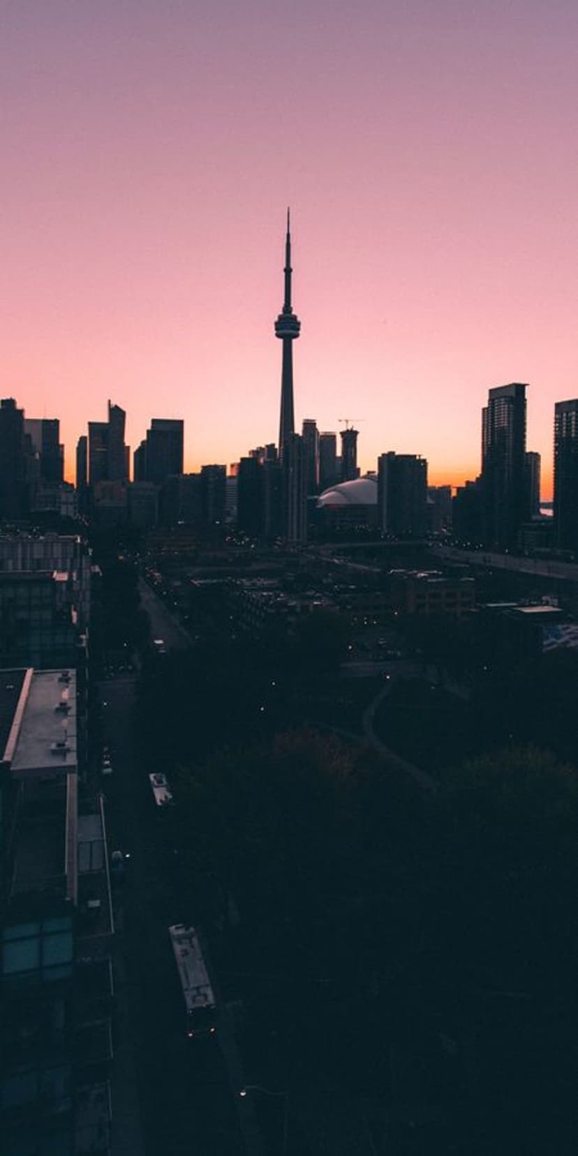 A tall communication tower silhouettes against a pink and orange sky above a darkened metropolitan skyline.