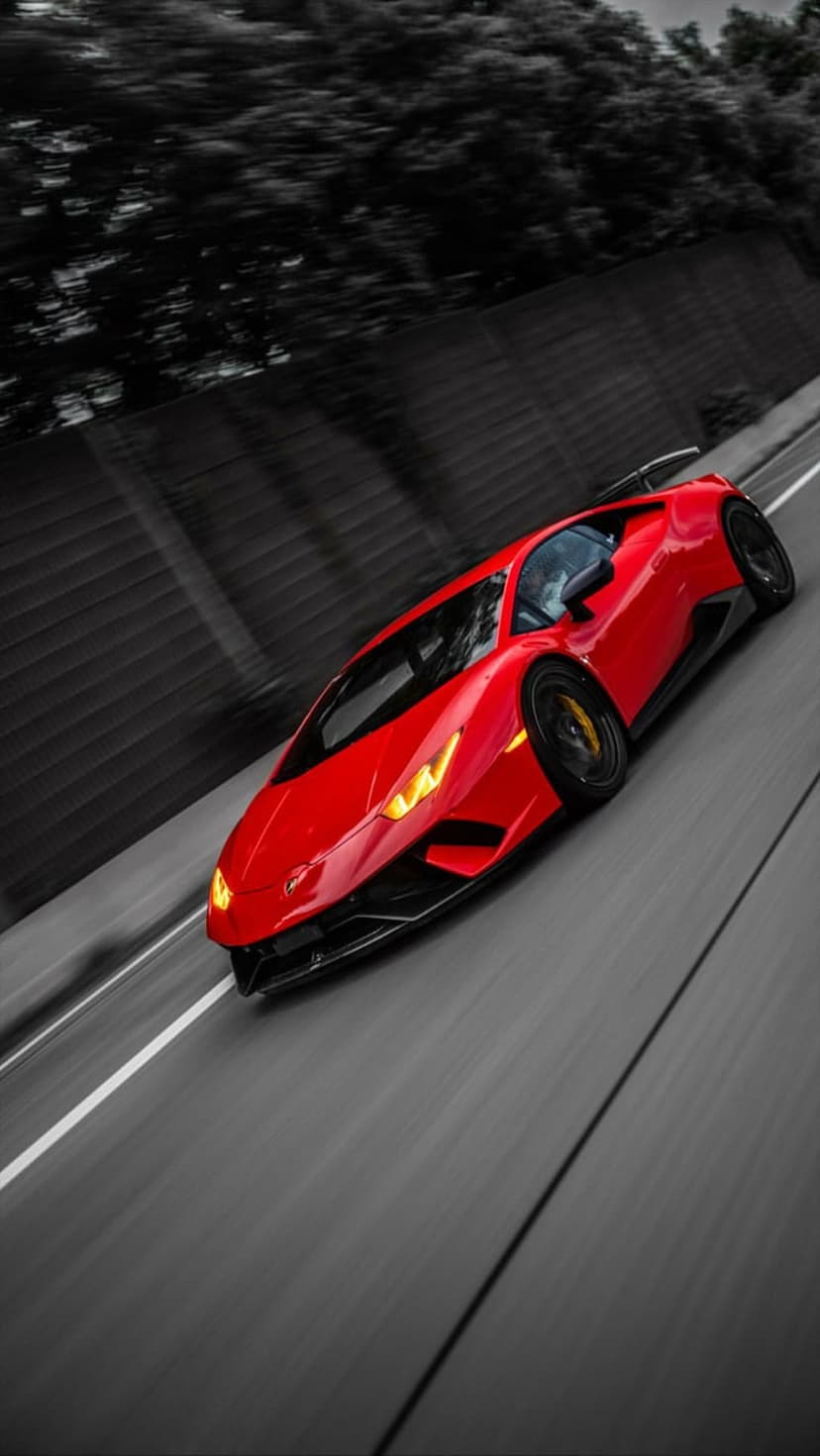 Red Lamborghini Huracan racing on a blurred asphalt highway with desaturated trees in the background.