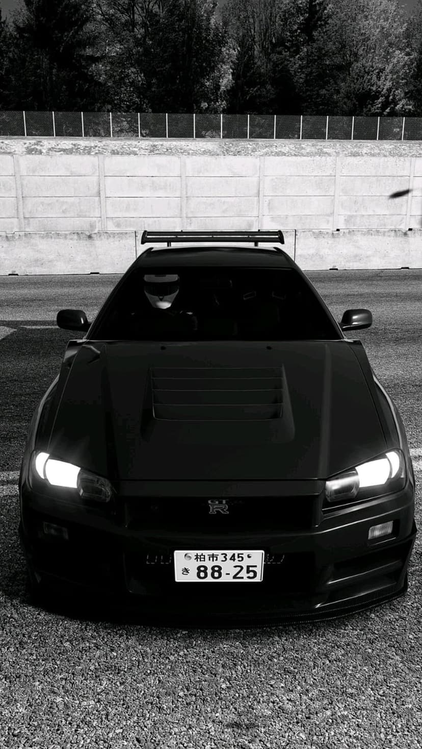 Black Nissan Skyline R34 GT-R with hood vents and a roof rack features glowing headlights in a dark setting.