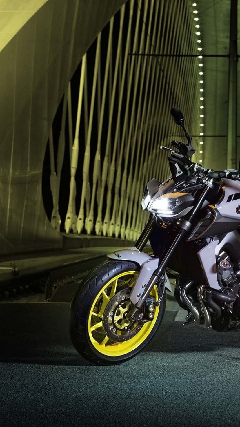 Yamaha motorcycle with neon yellow wheels and glowing headlights under architectural bridge cables at night.