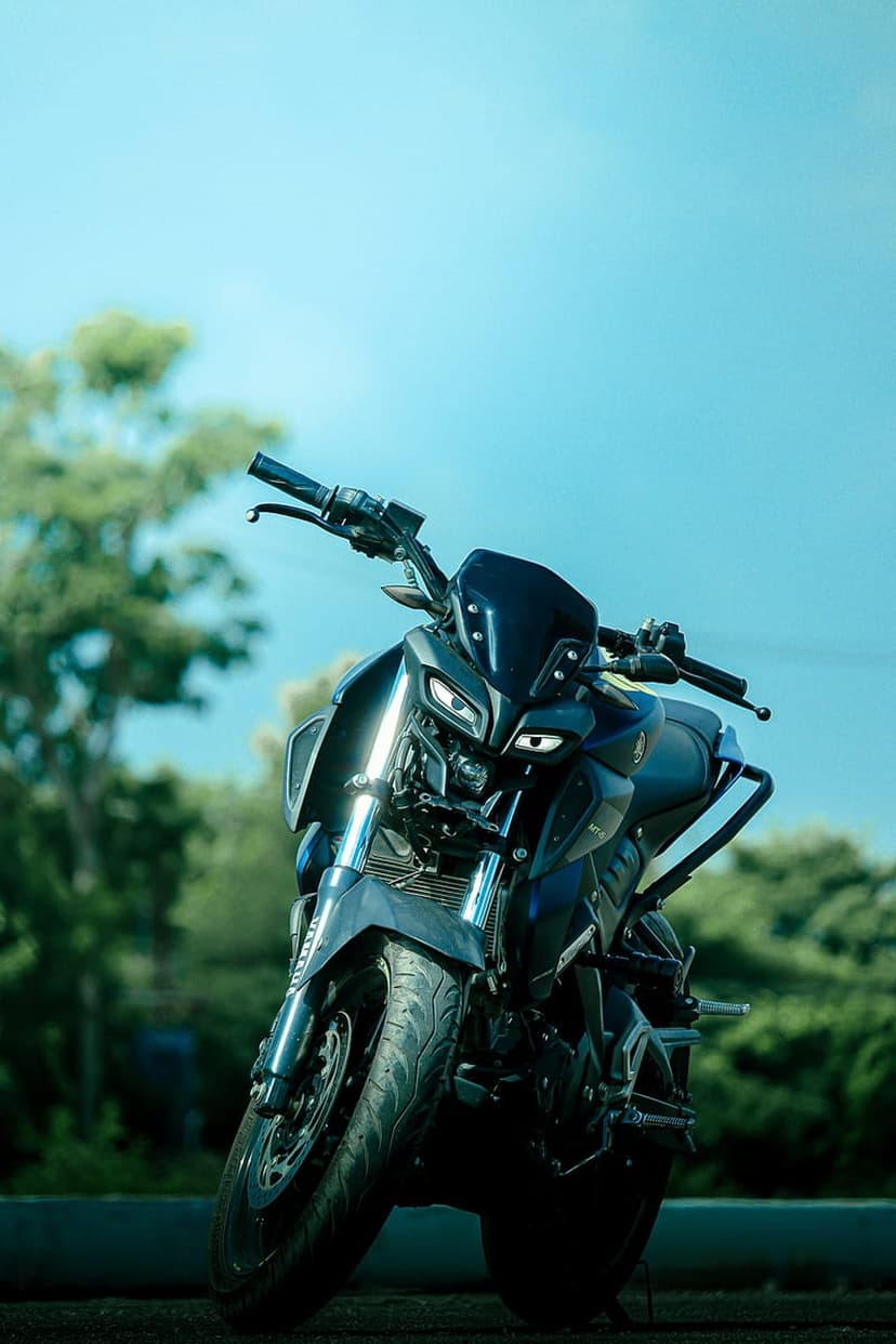 Yamaha MT-15 motorcycle with dual LED headlights, black windscreen, and textured tire under a bright blue sky.