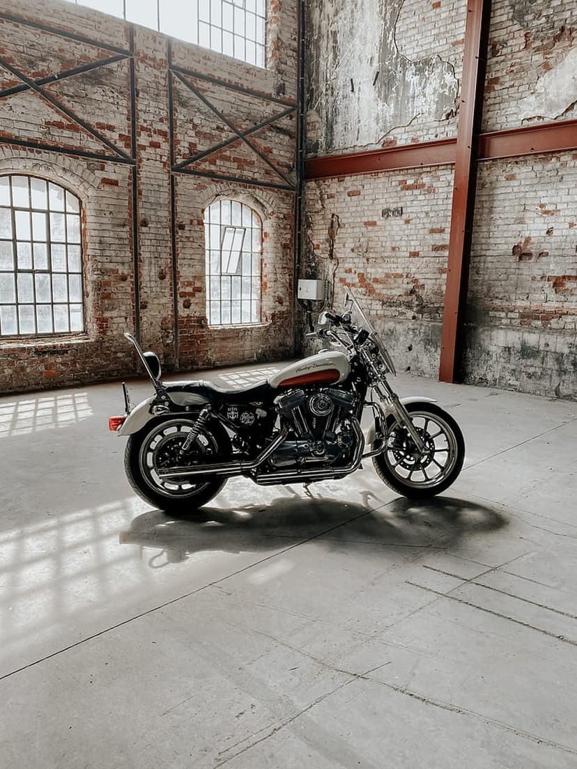 Harley Davidson motorcycle parked on concrete in a brick warehouse with sunlight streaming through large windows.