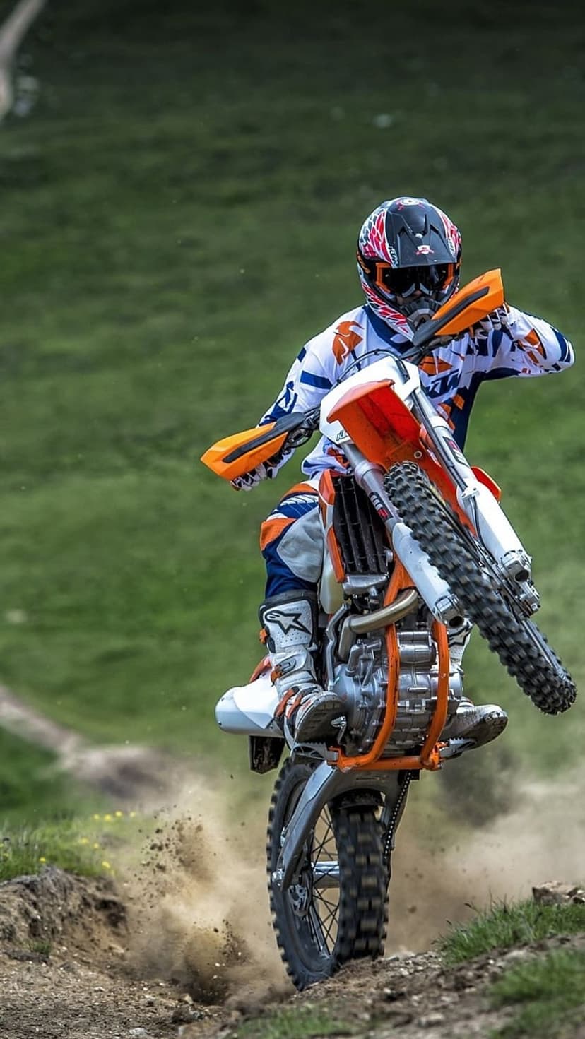Motocross rider wearing a helmet performs a mid-air jump on a dirt bike over a grassy outdoor racing track.