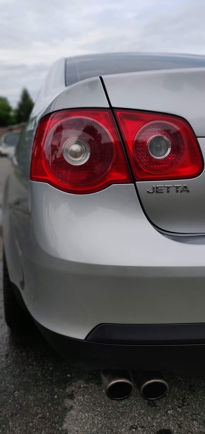 Silver Volkswagen Jetta rear tail lights and chrome dual exhaust pipes captured from a low angle perspective.