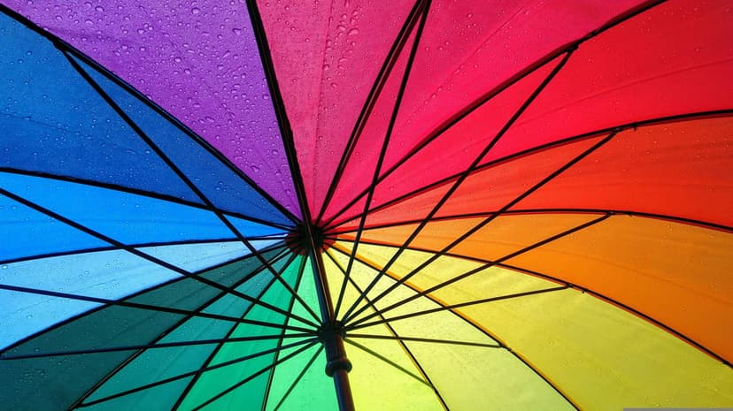 Rainbow umbrella canopy with glistening water droplets and visible spokes captured from a low-angle perspective.