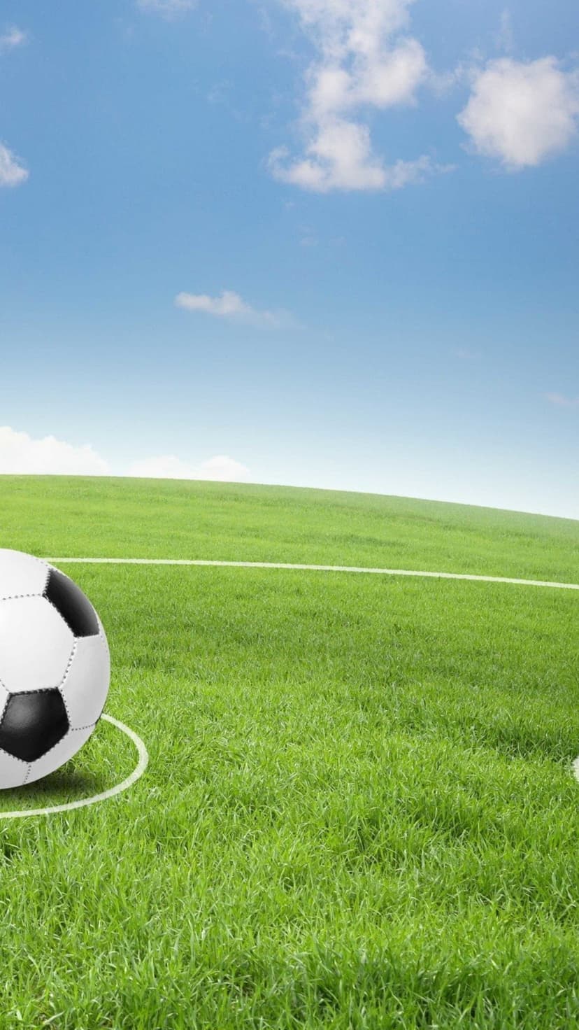 Black and white soccer ball sits on lush green grass with white boundary lines under a bright blue cloudy sky.