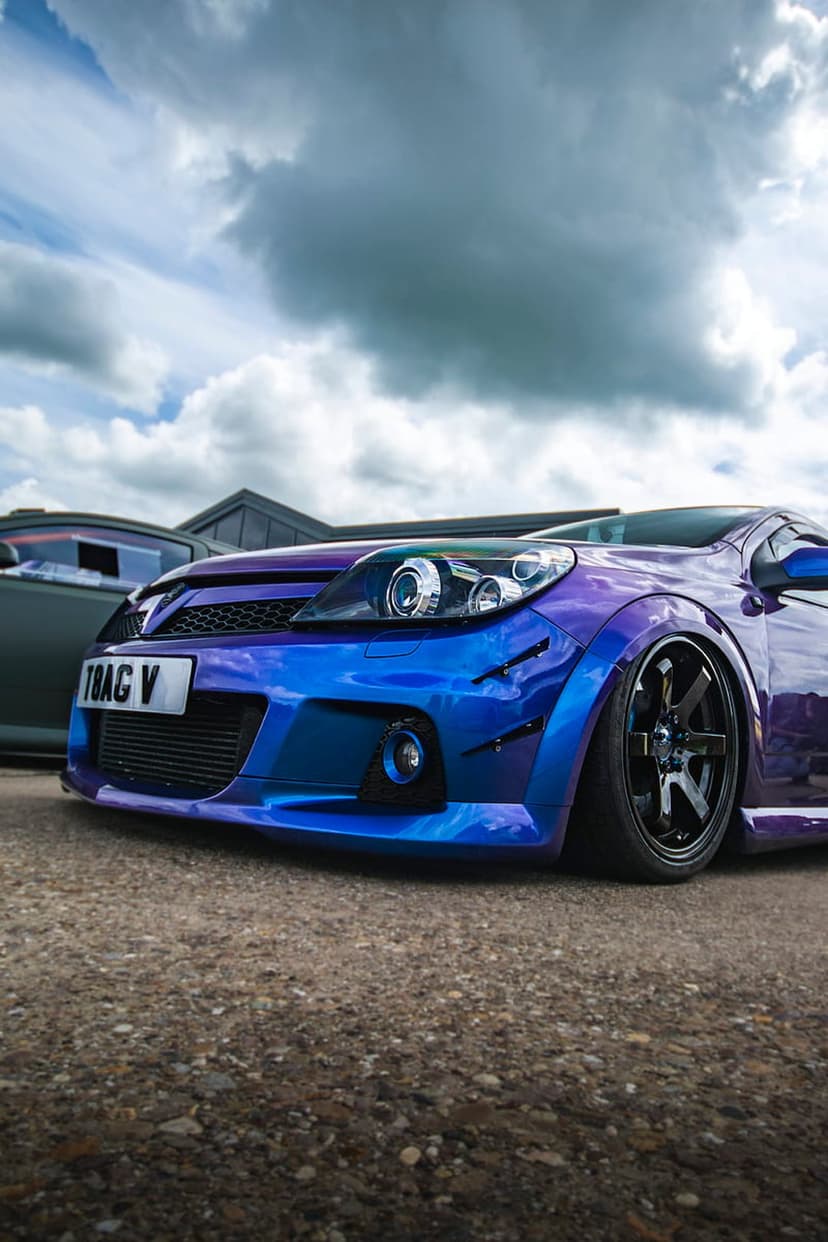 Modified car with iridescent blue and purple paint features wide fenders and black rims under a dramatic sky.