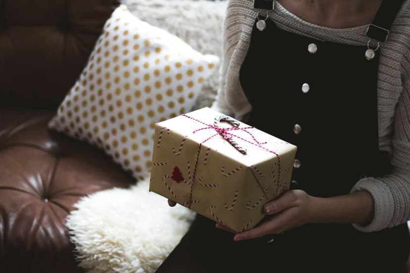 Person in a striped sweater holds a gift wrapped in brown paper with candy canes on a leather couch.