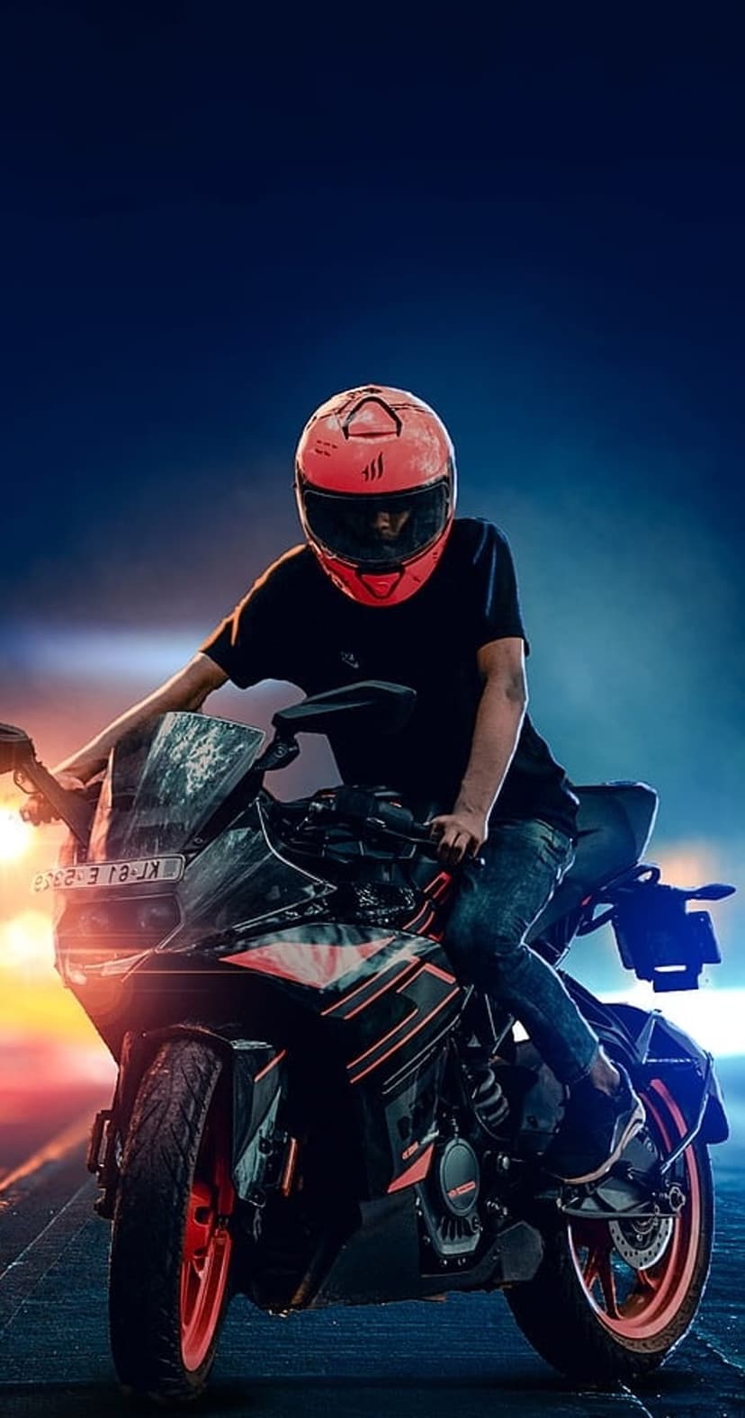 Motorcyclist in a red helmet on a black sportbike against a twilight sky with orange and blue horizon gradients.