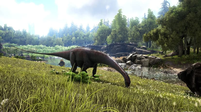 Long-necked dinosaur grazing in a lush green meadow beside a river with a dense forest background under a hazy sky.