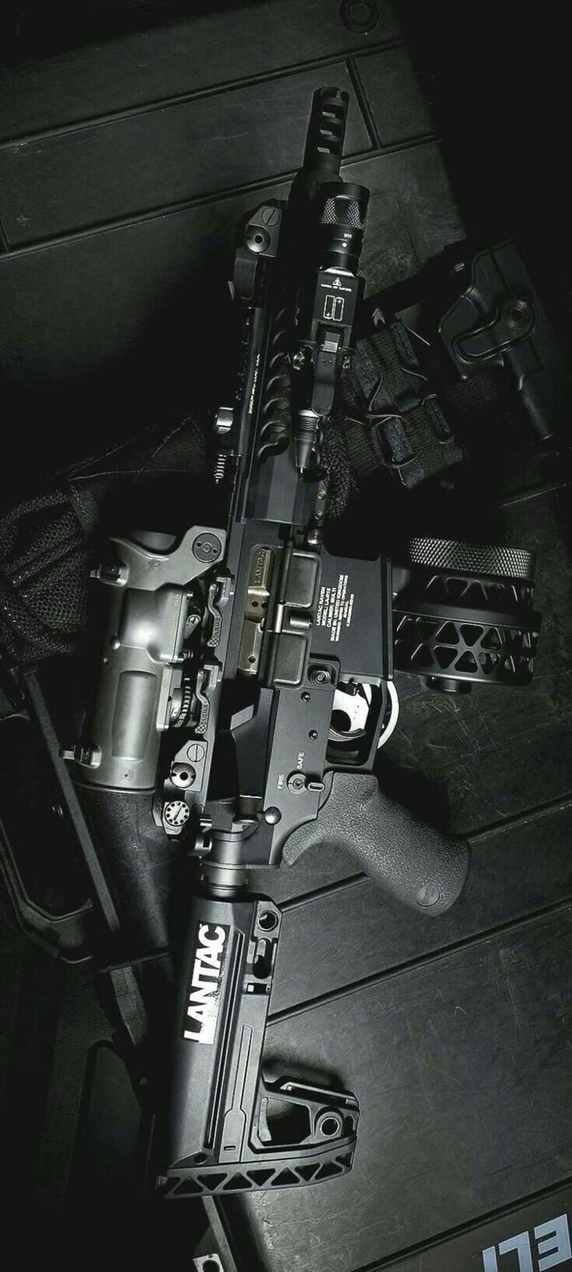 Tactical AR-15 rifle with a drum magazine and Magpul grip on a dark textured surface in vertical orientation.