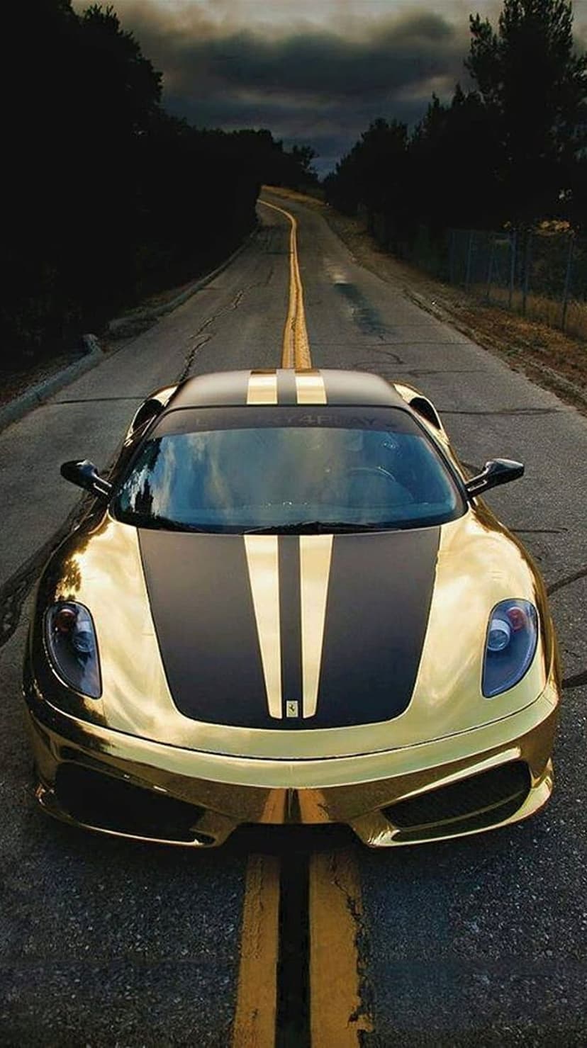 Golden Ferrari supercar with black racing stripes driving on a wet winding road under a dark stormy sky at dusk.