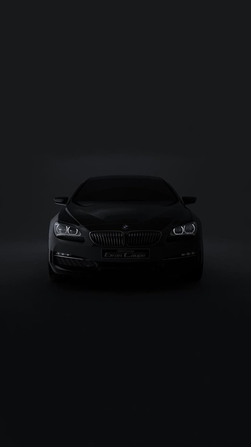 BMW Gran Coupe front view in dark lighting with glowing white headlights and a chrome kidney grille visible.