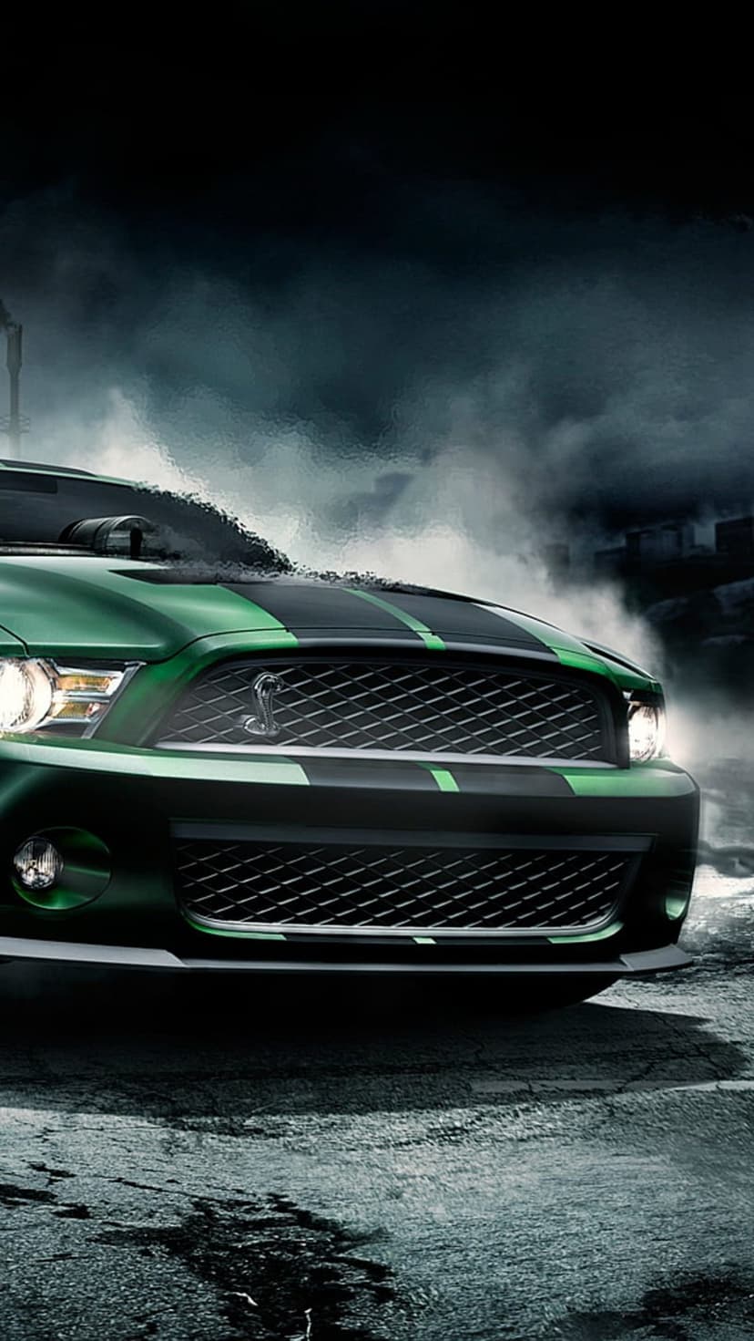 Green Mustang Shelby GT500 with black stripes drives on wet asphalt through thick white smoke at night.