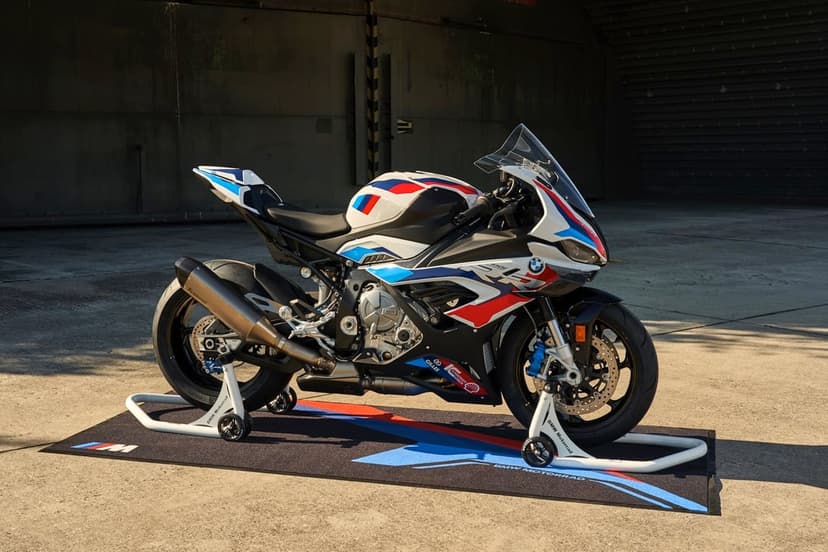 BMW M 1000 RR motorcycle mounted on white paddock stands against an industrial hangar background.