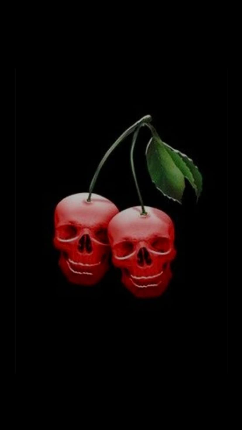 Red skull-shaped cherries with a green leaf suspended against a solid black background in a macabre still life.
