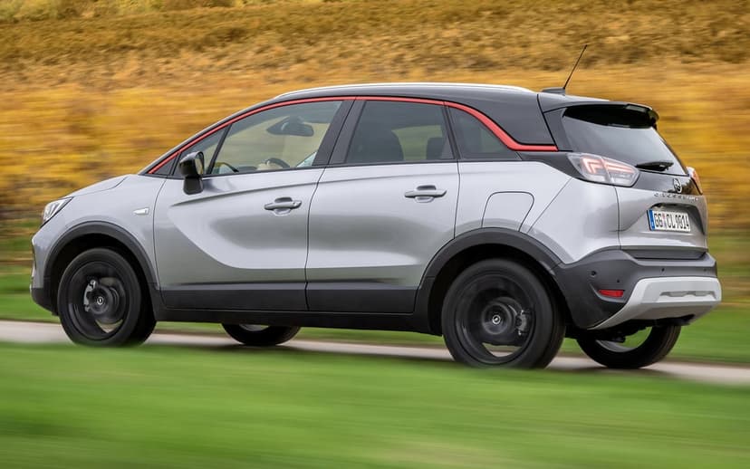 Silver Opel Crossland SUV driving on a road with motion blurred wheels and a yellow hillside background.