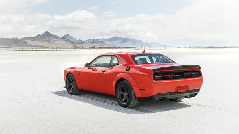 Red Dodge Challenger SRT Demon parked on vast white salt flats with distant mountains under a cloudy sky.