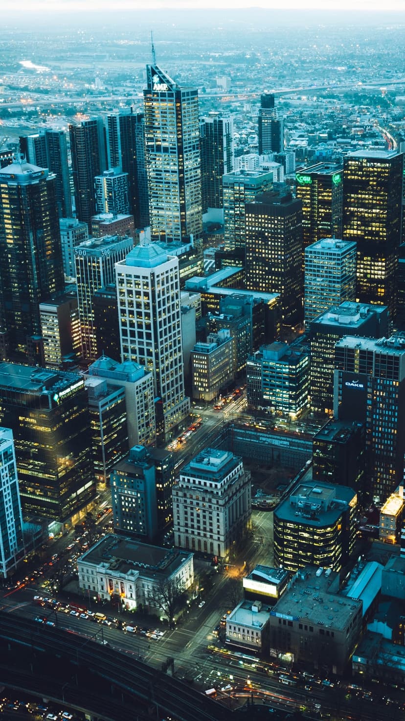 Luminous skyscrapers and glowing traffic streaks viewed from above create a geometric urban grid at dusk.
