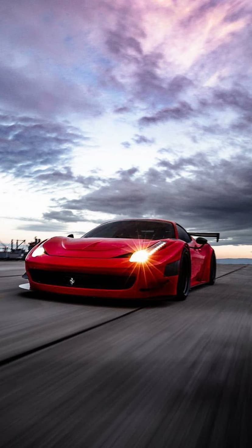 Red Ferrari 458 Italia supercar with glowing headlights racing on a road under a purple and pink sunset sky.