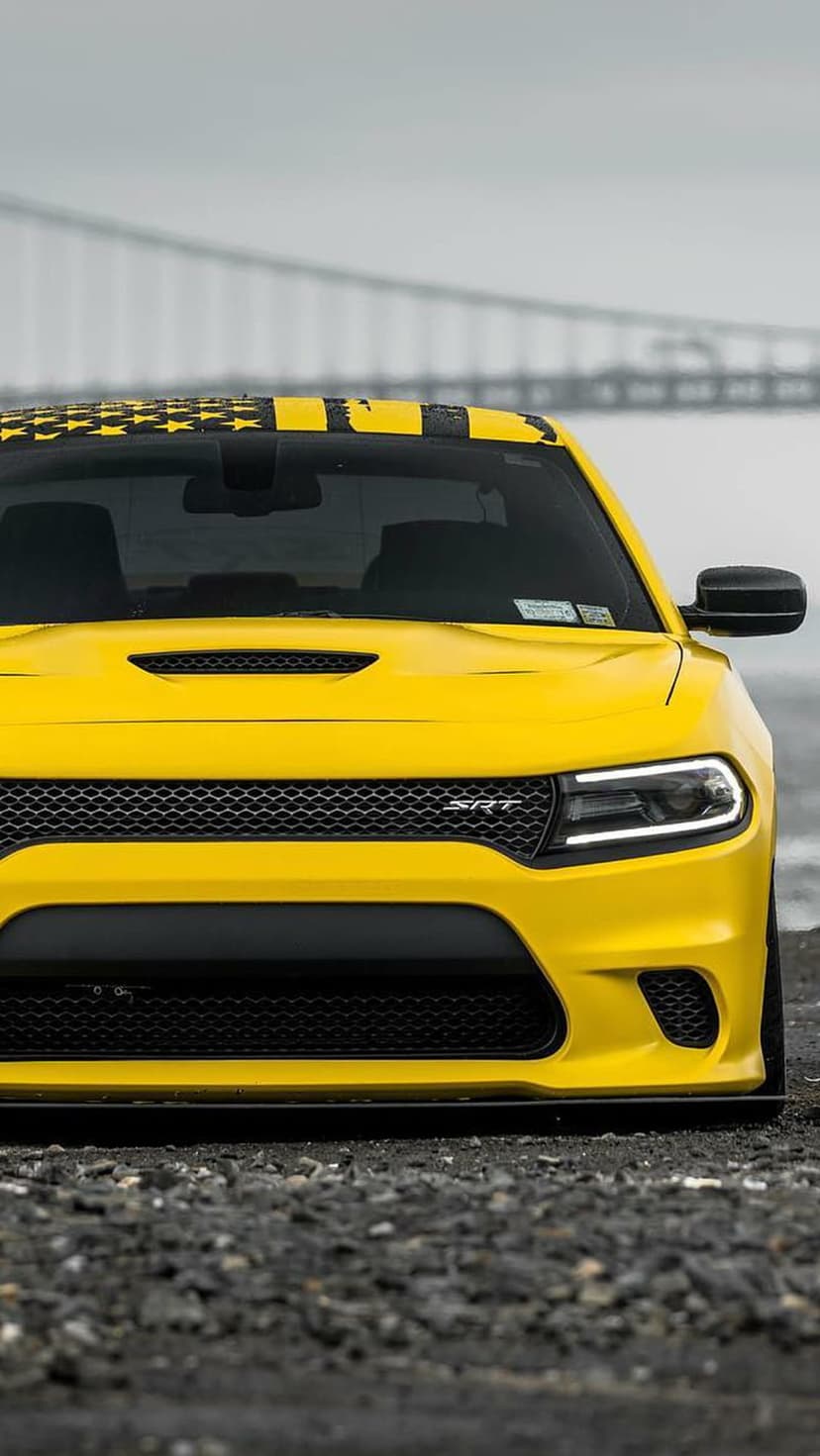 Yellow Dodge Charger SRT with American flag decals on a bridge, featuring an aggressive front grille and headlights.