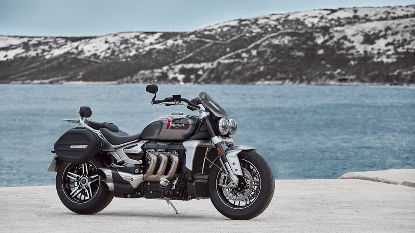 Triumph Rocket 3 GT motorcycle parked on a pier overlooking blue water and snowy coastal mountains.
