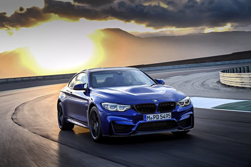 Blue BMW sports car driving on a racetrack at sunset with motion blur, mountains, and golden light.