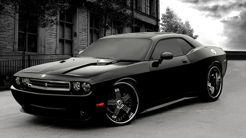 Black Dodge Challenger parked on a city street with custom rims and a single orange side marker light.