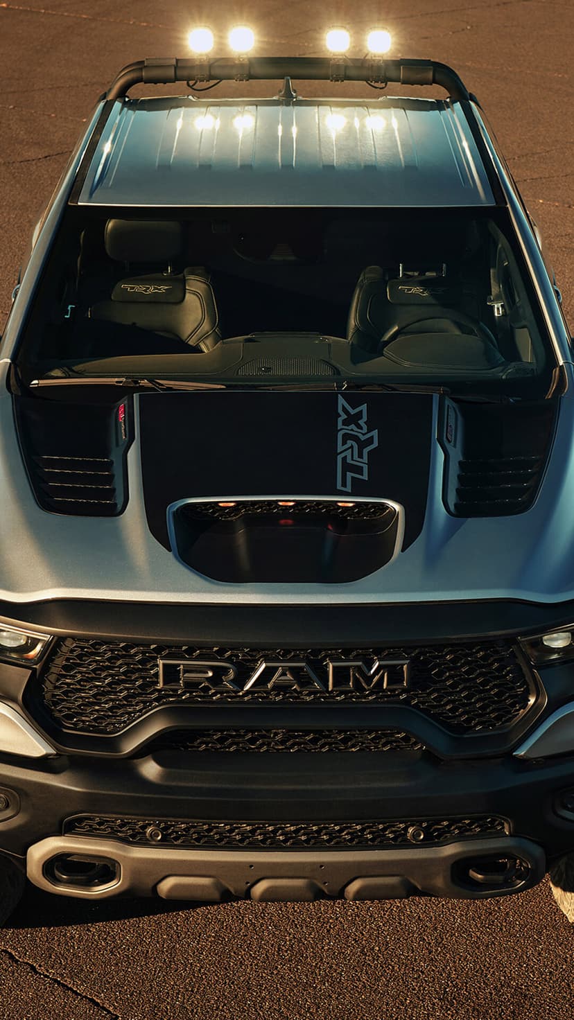 Silver Ram 1500 TRX truck front view with roof lights, TRX hood graphics, and black grille at sunset.