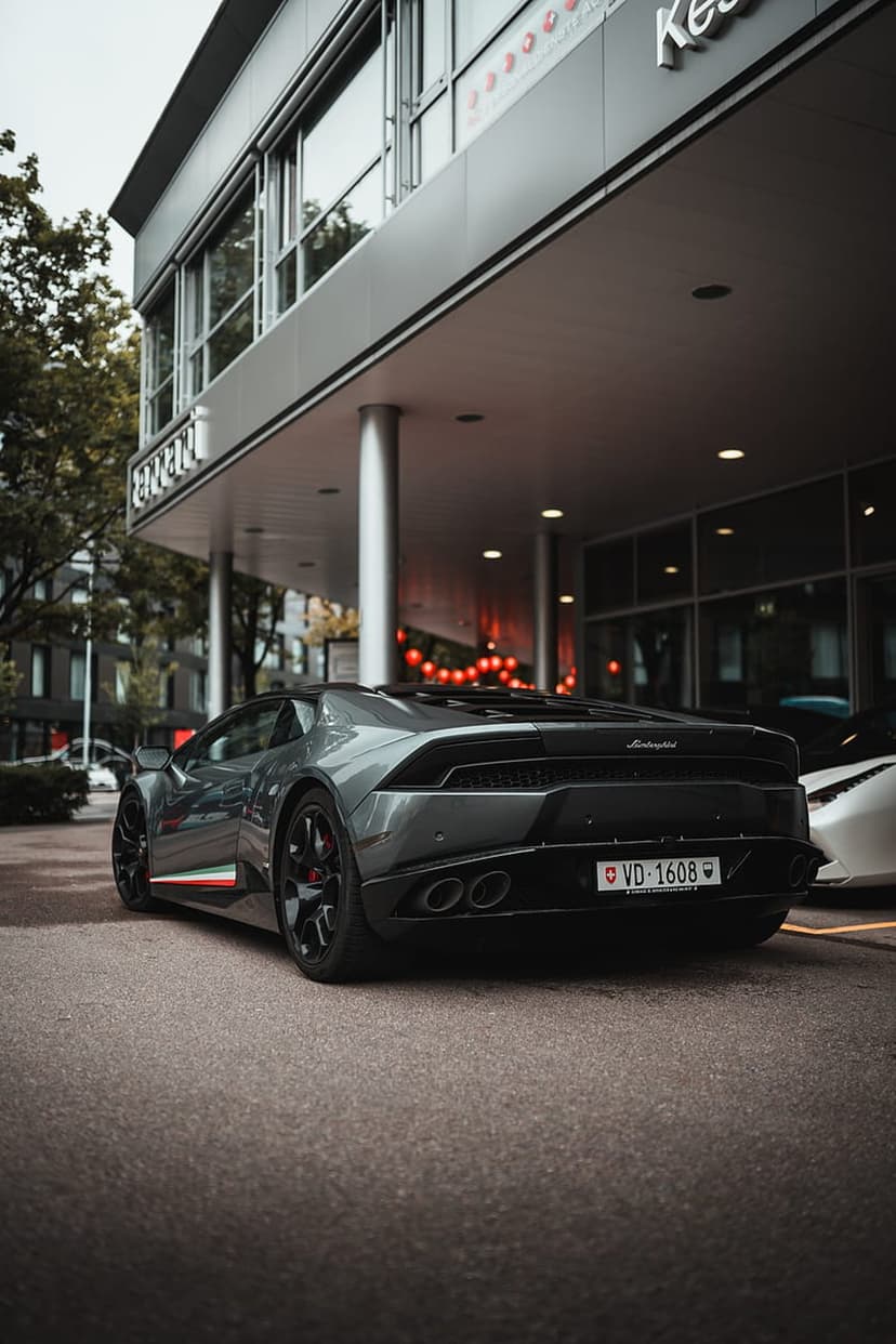 Gray Lamborghini Huracan with Italian flag stripes parked beside a minimalist silver and glass office building.