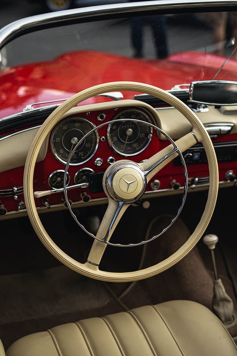 White Mercedes-Benz 300 SL steering wheel with a chrome emblem inside a red leather cabin with analog gauges.