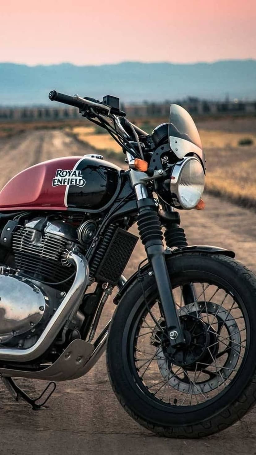 Royal Enfield Interceptor 650 with a maroon tank parked on a dirt road under a soft pink sunset sky.