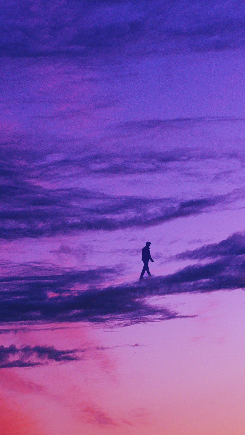 Person silhouette walking on dark clouds against a vibrant purple and pink sky in a vertical perspective.