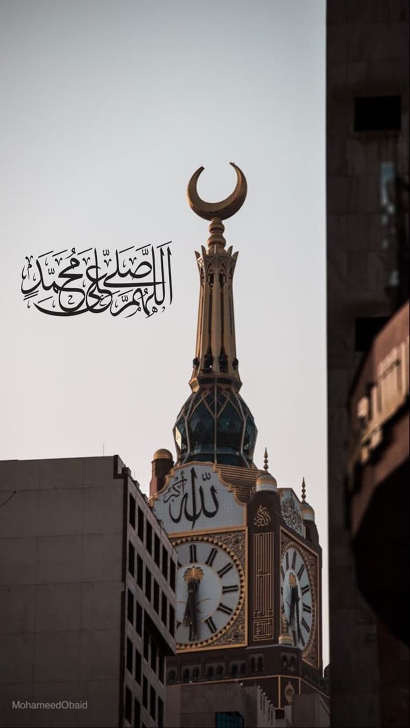 Makkah Clock Tower with gold Arabic calligraphy, large clock faces, and a crescent moon finial under a blue sky.