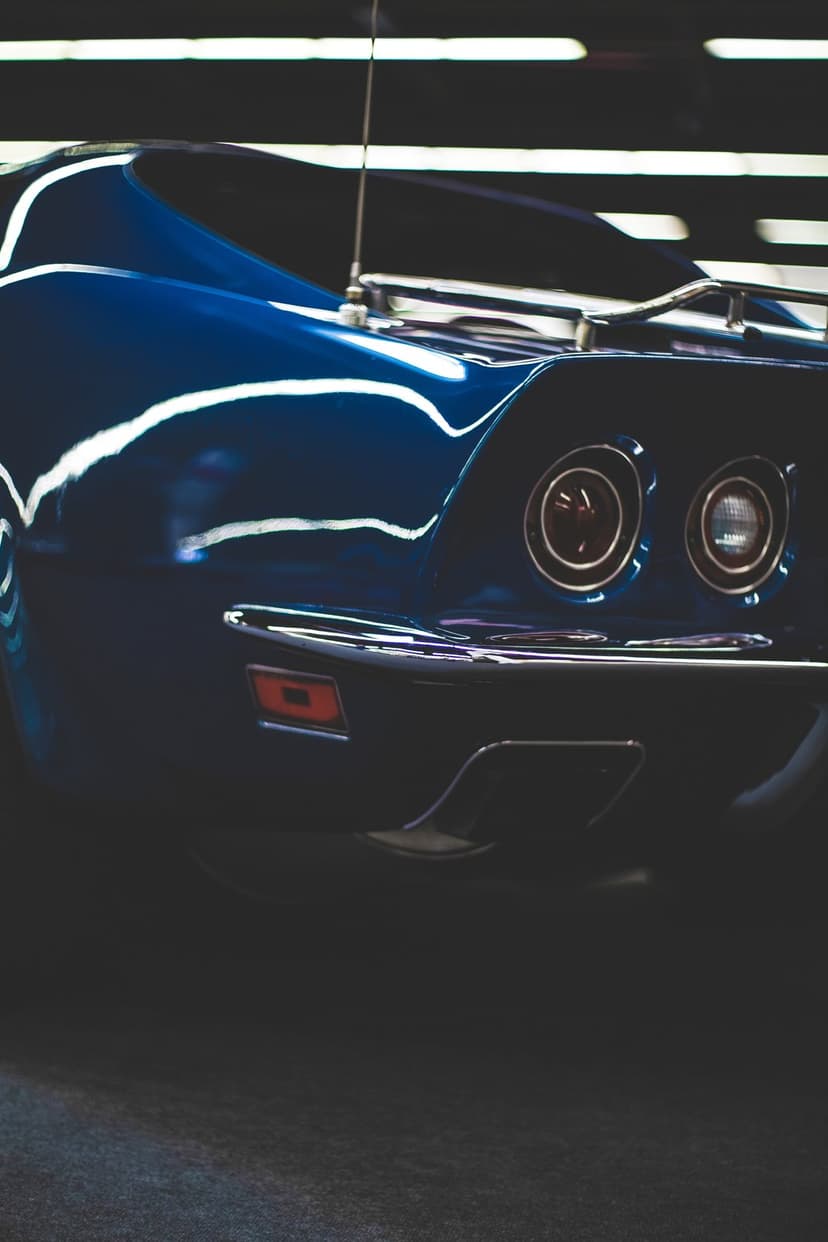 Blue Corvette tail lights and a polished chrome bumper reflect soft lights in a detailed low-angle car close-up.