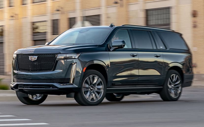 Cadillac Escalade luxury SUV driving on a city street with motion blurred wheels and golden hour reflections.