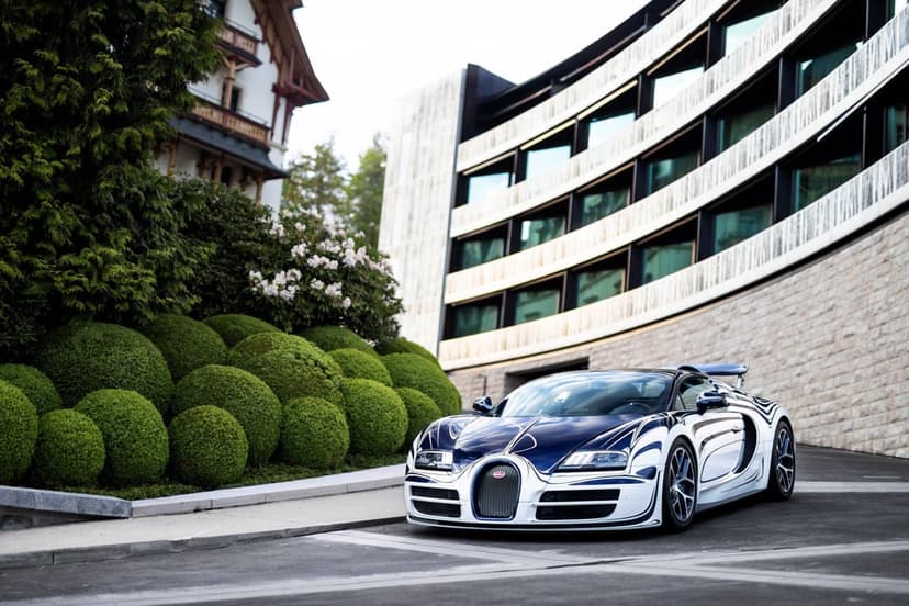 Bugatti Veyron L'Or Blanc with blue swirls parked near green topiary and a modern curved building.