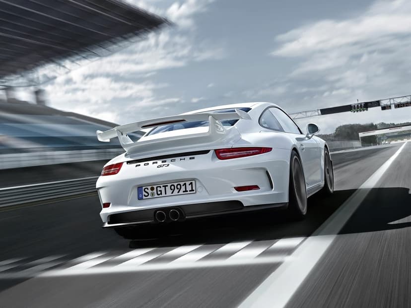 White Porsche 911 GT3 driving fast on a racetrack with motion blur background and signature rear wing visible.