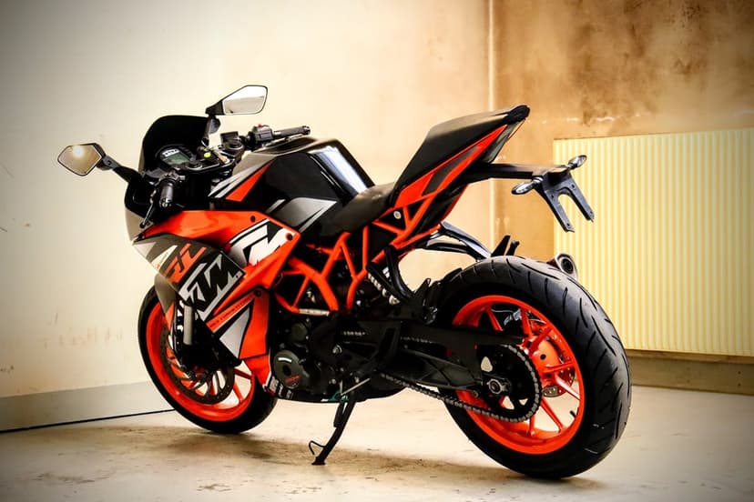 Orange and black KTM sportbike with a trellis frame and bright orange wheels parked against a beige wall.