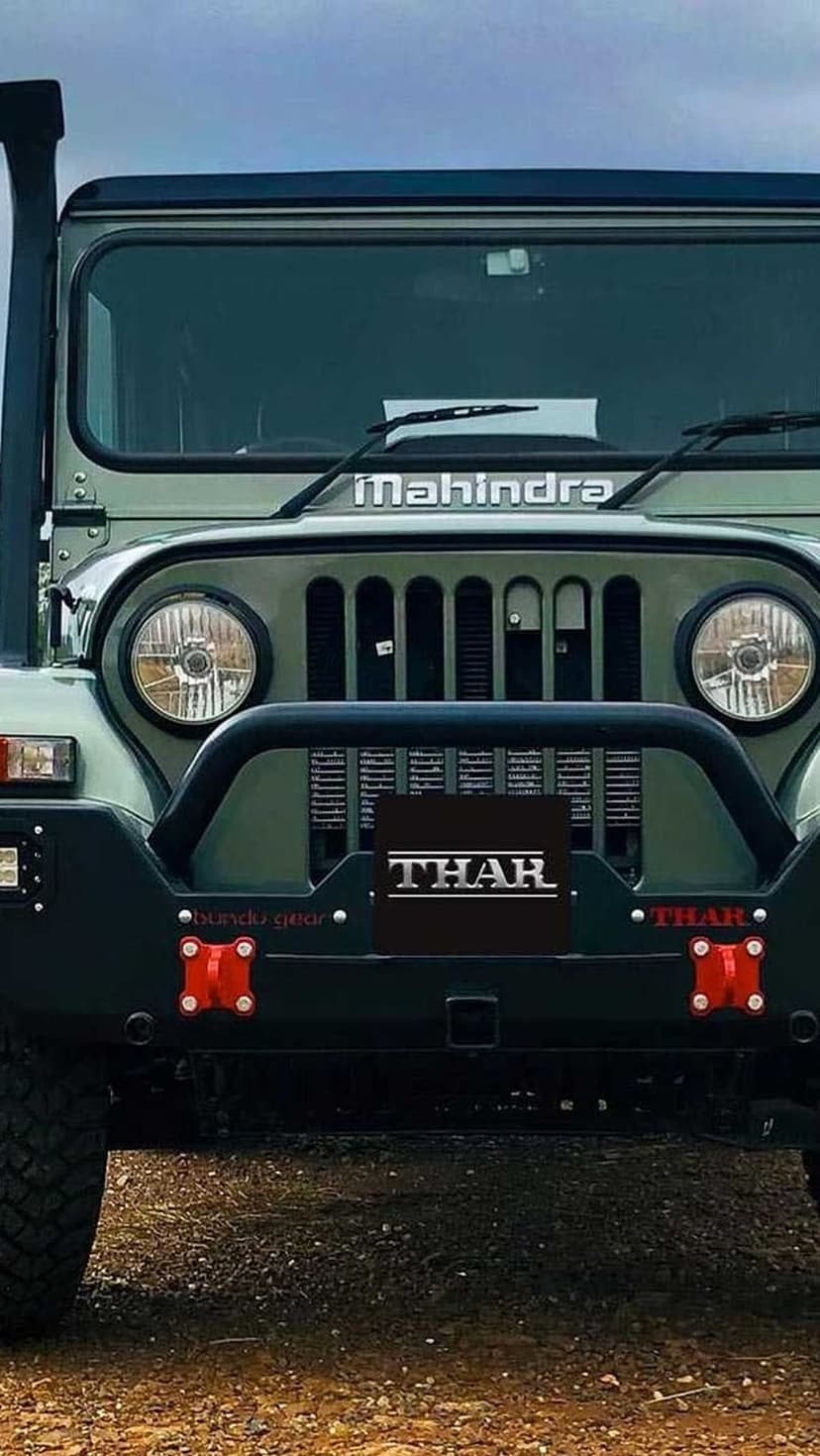 Mahindra Thar off-road vehicle with a green finish, round headlights, and red tow hooks on a gravel surface.