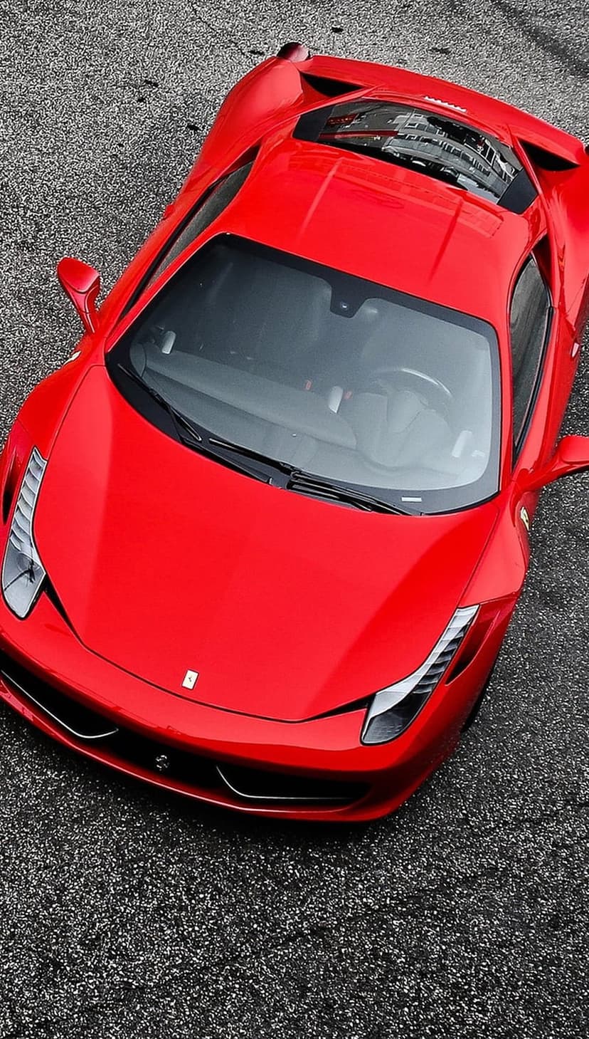 Red Ferrari 458 Italia supercar viewed from above on textured gray asphalt with visible headlight details.