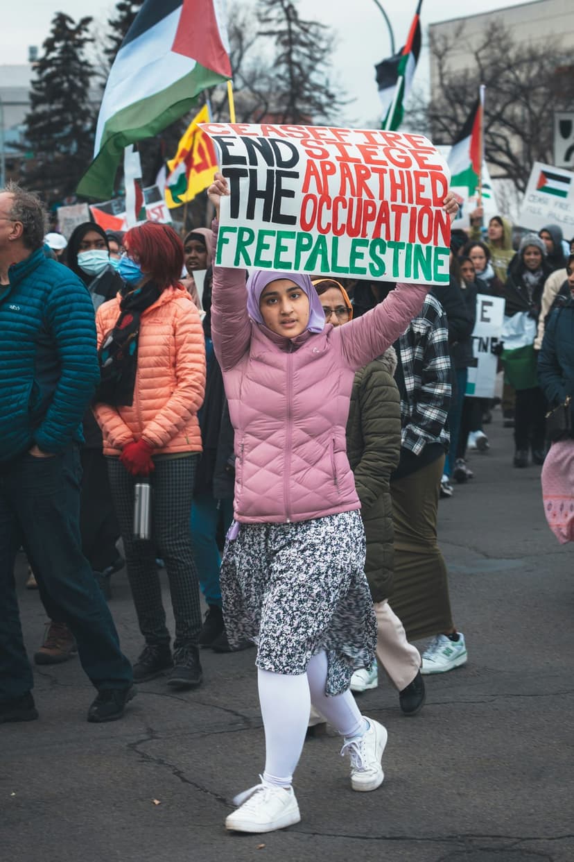 Young woman holding an activist sign during a Palestinian solidarity march with flags blurred in the background.