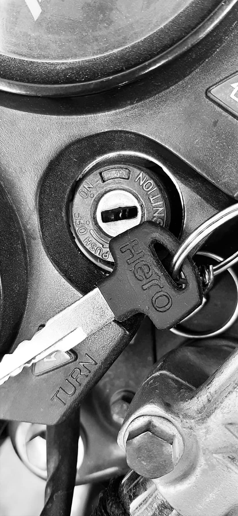Motorcycle ignition key with Hero logo and dashboard controls captured in high-contrast black and white photography.