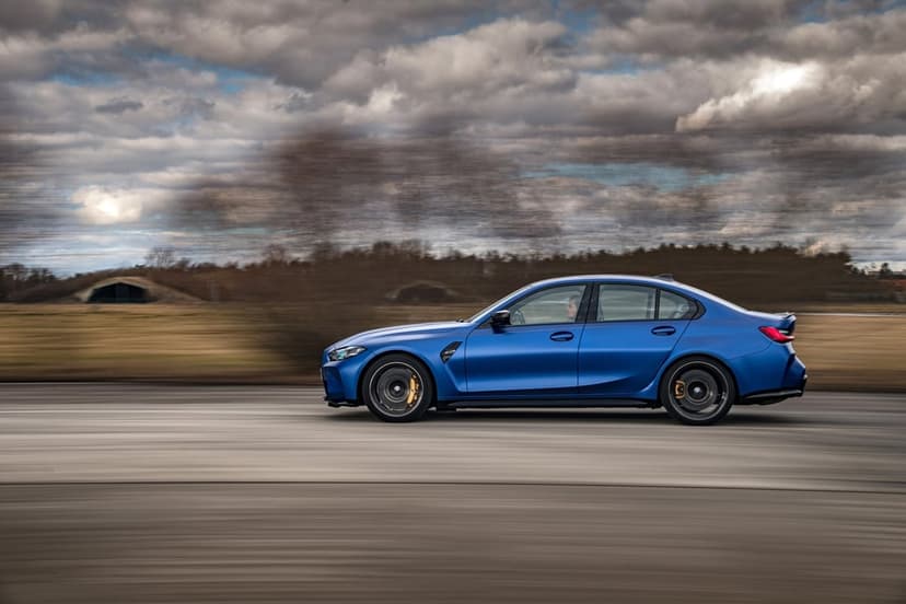 Side view of a blue BMW M3 speeding on a track with motion blur against a dramatic cloudy sky and gold brakes.