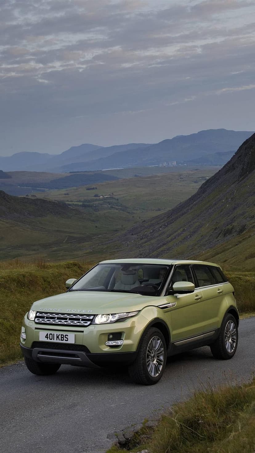 Range Rover Evoque with glowing headlights driving on a winding road through steep, misty Welsh mountains.
