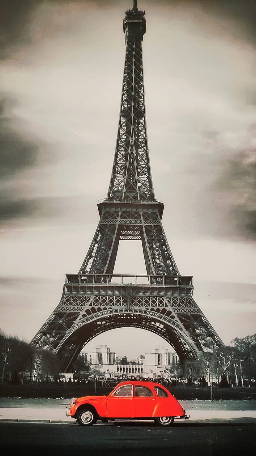 Red vintage car parked on a Parisian street with the black and white Eiffel Tower rising in the background.