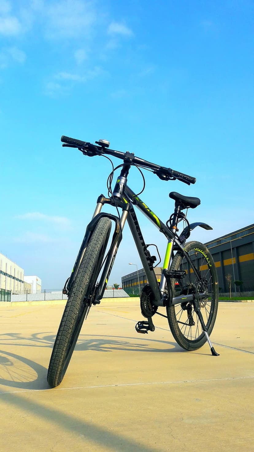 Black mountain bike with neon green accents on concrete against a blue sky with clouds in a low-angle view.