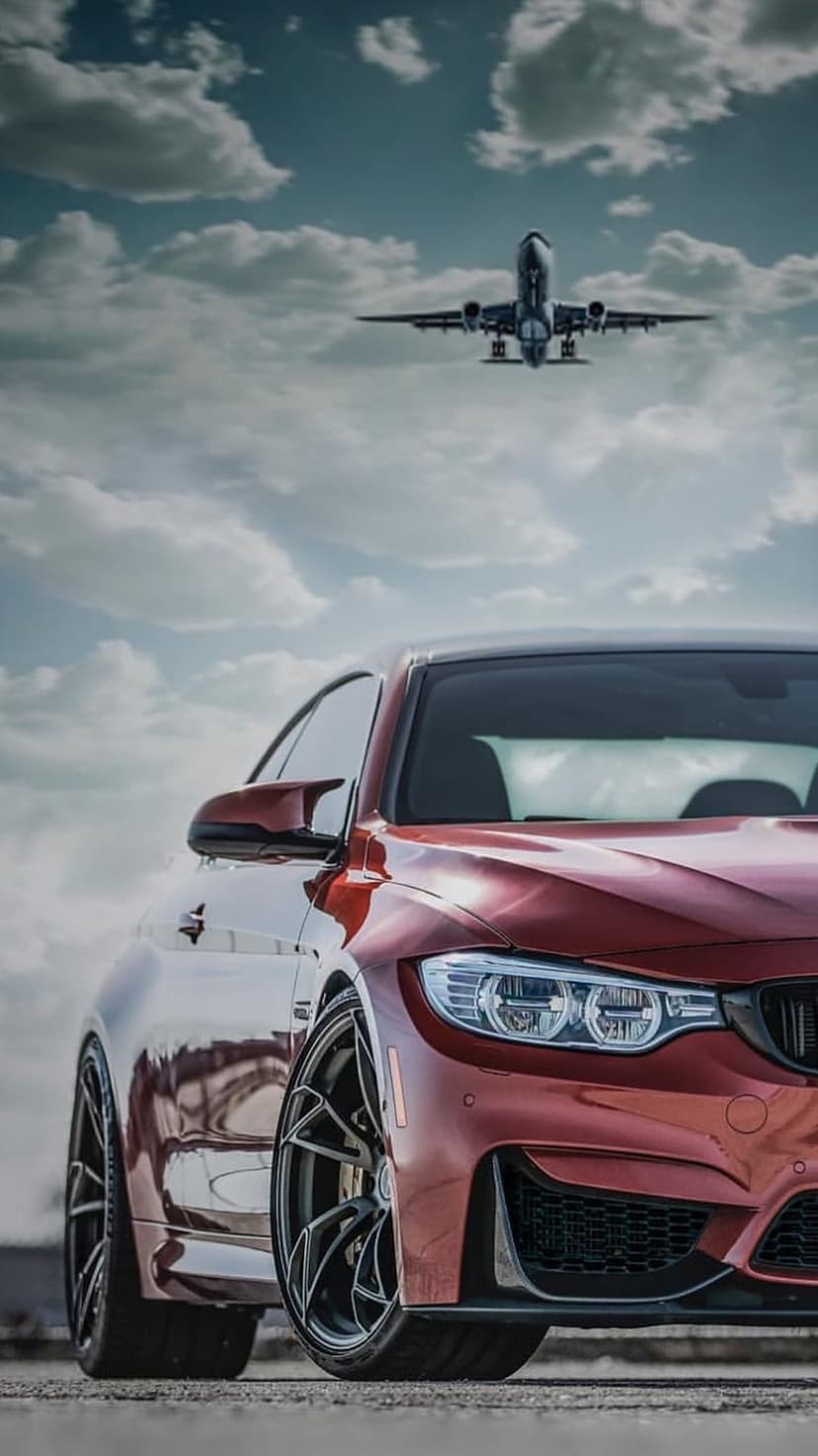 Red sports car parked on tarmac while a large commercial airplane flies through heavy clouds in a dramatic sky.