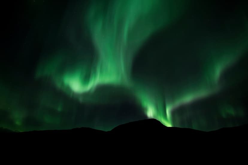 Vibrant green aurora borealis streaks across a starry night sky above sharp, black mountain silhouette peaks.