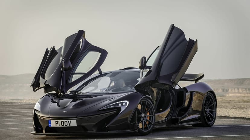 Dark purple McLaren P1 hypercar with butterfly doors open parked on asphalt against a hazy desert background.